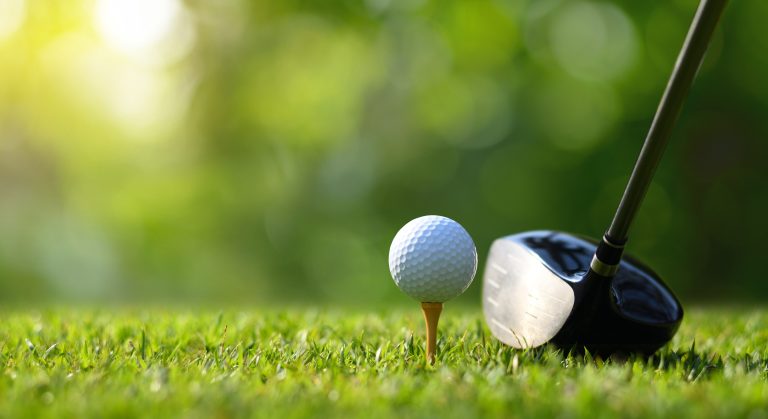 Close-up golf ball on tee with golf drivers at golf course.
