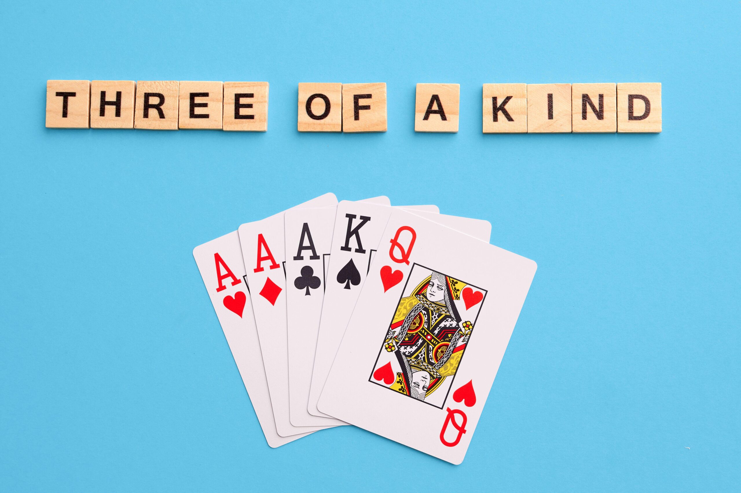 2J53TGX Three of a kind combination. Poker Playing Cards on blue background with wooden blocks. Flatlay, copy space, concept